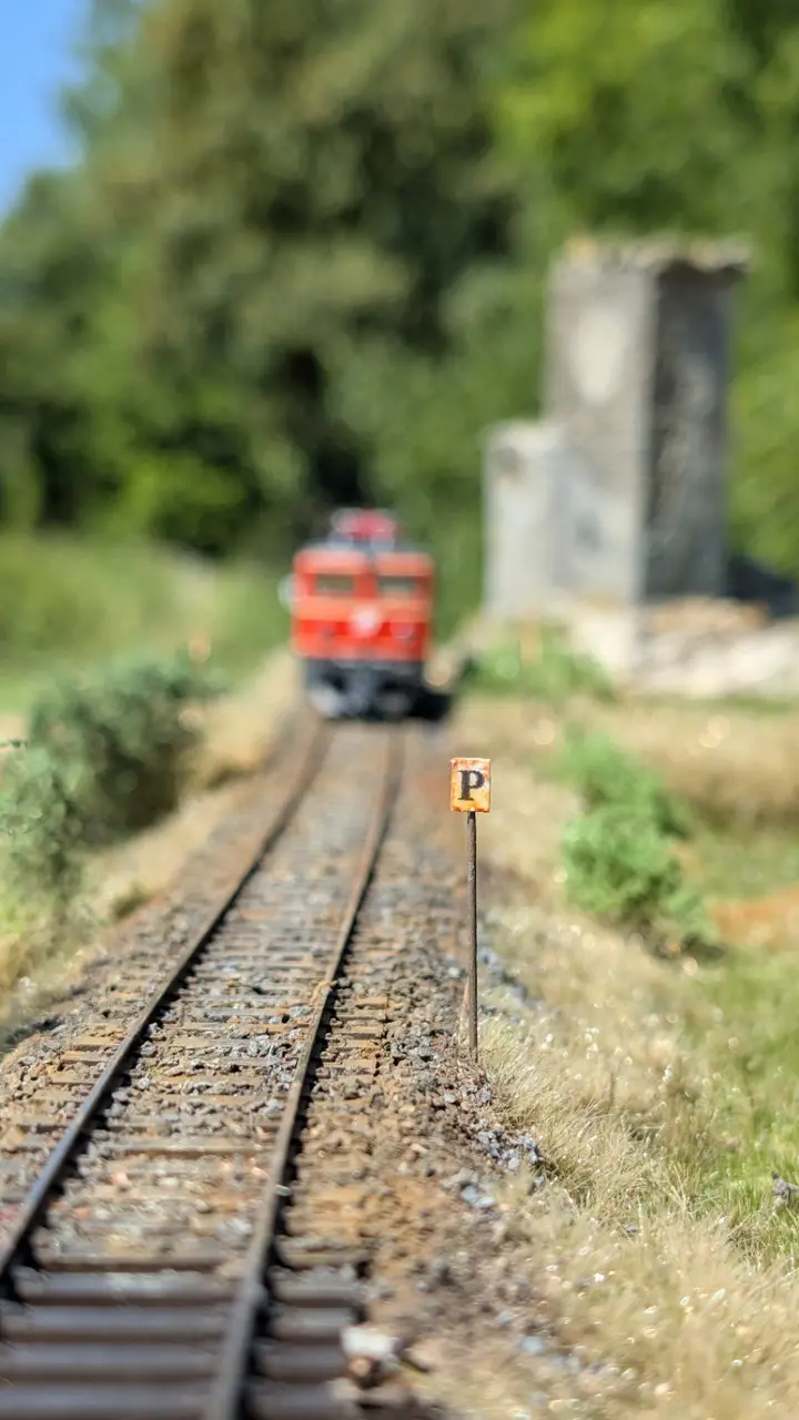 Gleis mit Signaltafel und roter Lok im Hintergrund