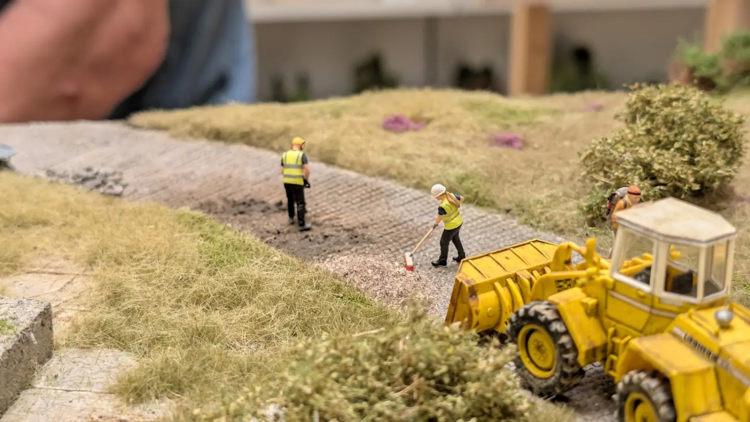 Gesamtansicht einer Pflasterstra&szlig;en-Baustelle mit Schrumpfmich-Figuren und gelbem Radlader
