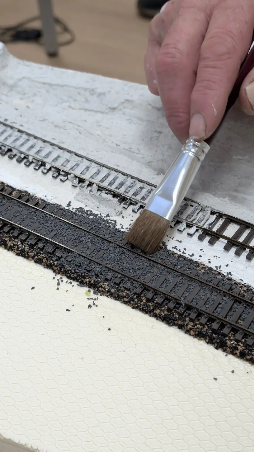 Detailaufnahme beim Einschottern des Gleises mit einem weichen Pinsel
