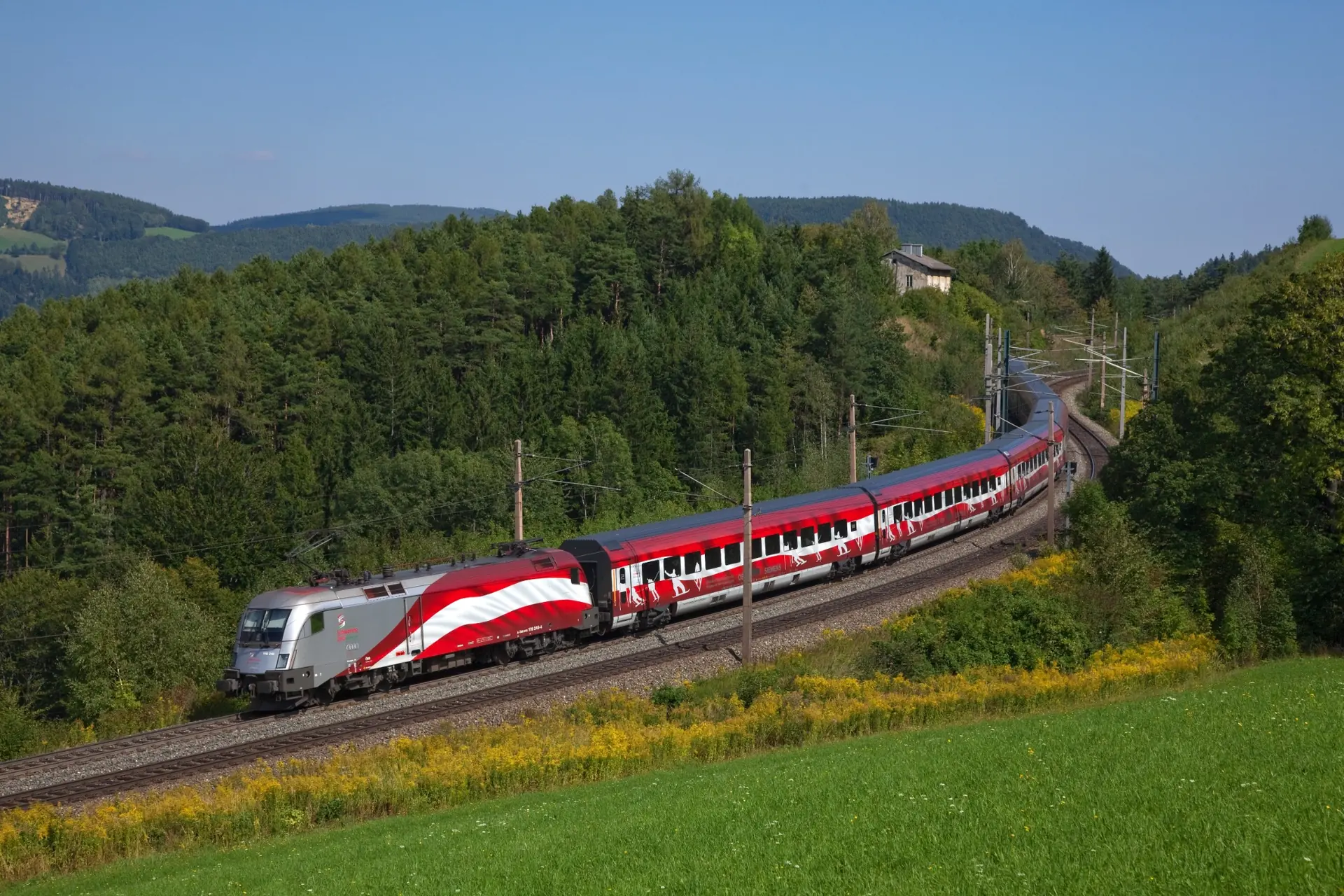 Vorbildaufnahme eines Reisezuges in einem weiten Gleisbogen durch eine Berglandschaft