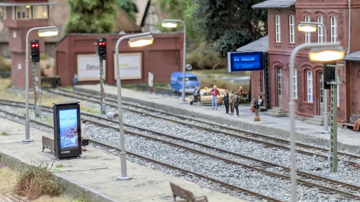 Bahnsteigszene mit Werbes&auml;ule und Zugzielanzeiger in einer Blickachse